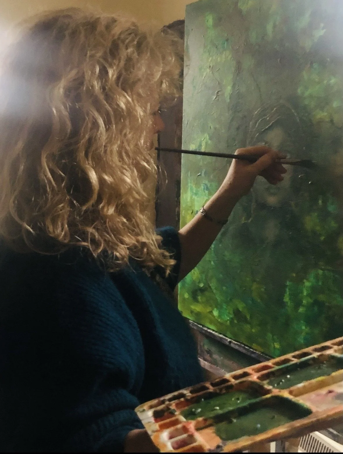 A woman with curly blonde hair painting a landscape on an easel.