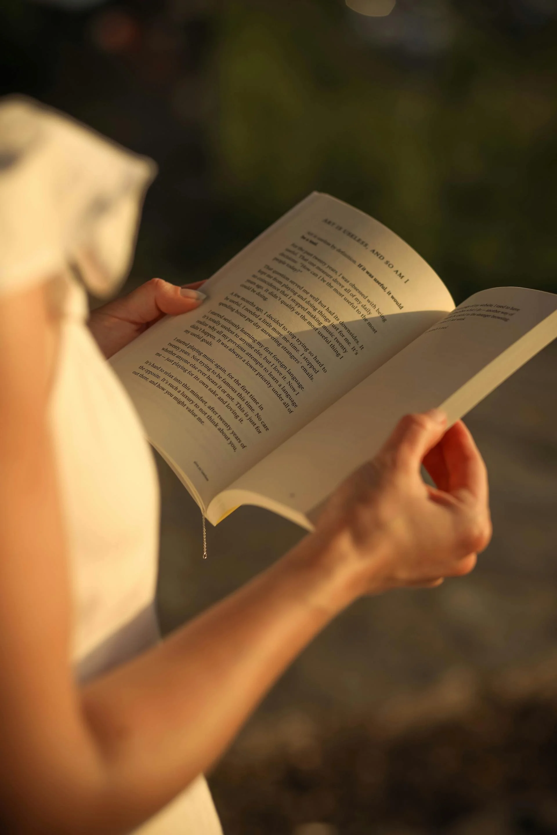 Close-up of a person holding an open book outdoors with a blurred dark background.