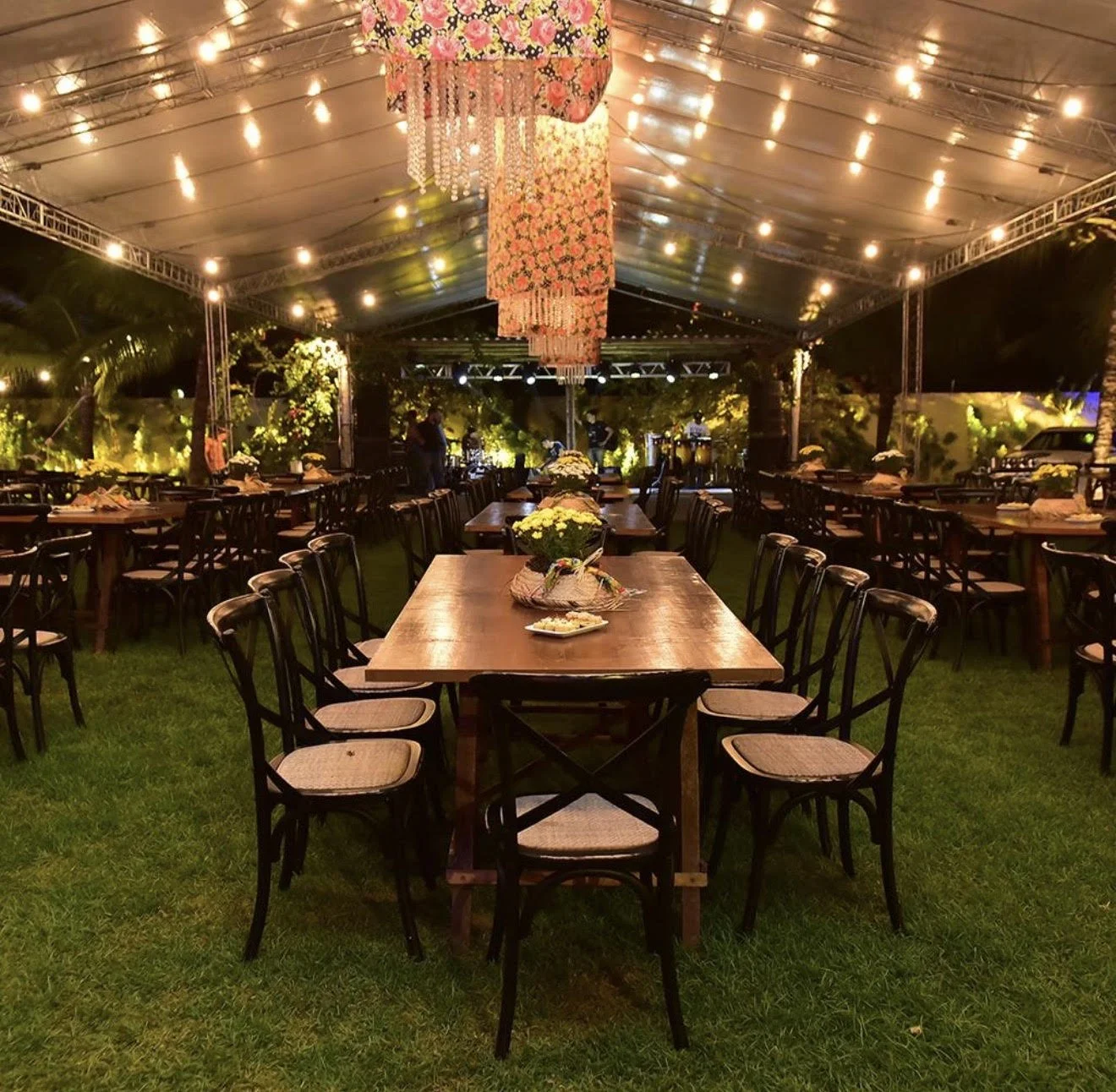 Decorated outdoor event tent at night with neatly arranged tables and chairs, floral centerpieces, and string lights, set up for a celebration or gathering.