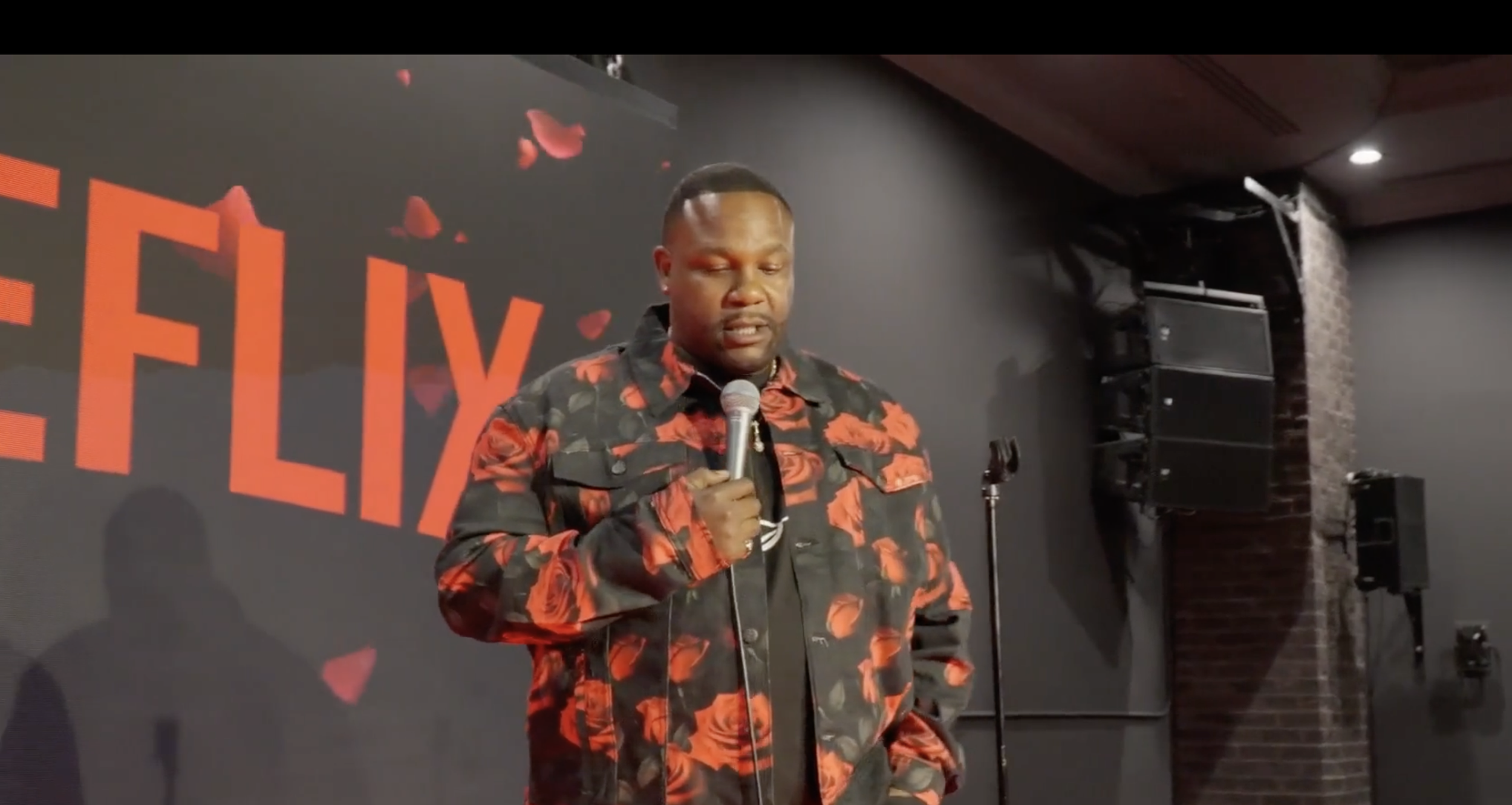 A man with a microphone performing on stage at a Valentine's Day event, with a large screen displaying 'FLIX' and Valentine hearts in the background.