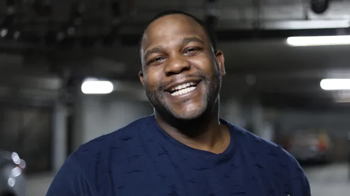 A smiling man in a blue shirt standing in a parking garage.