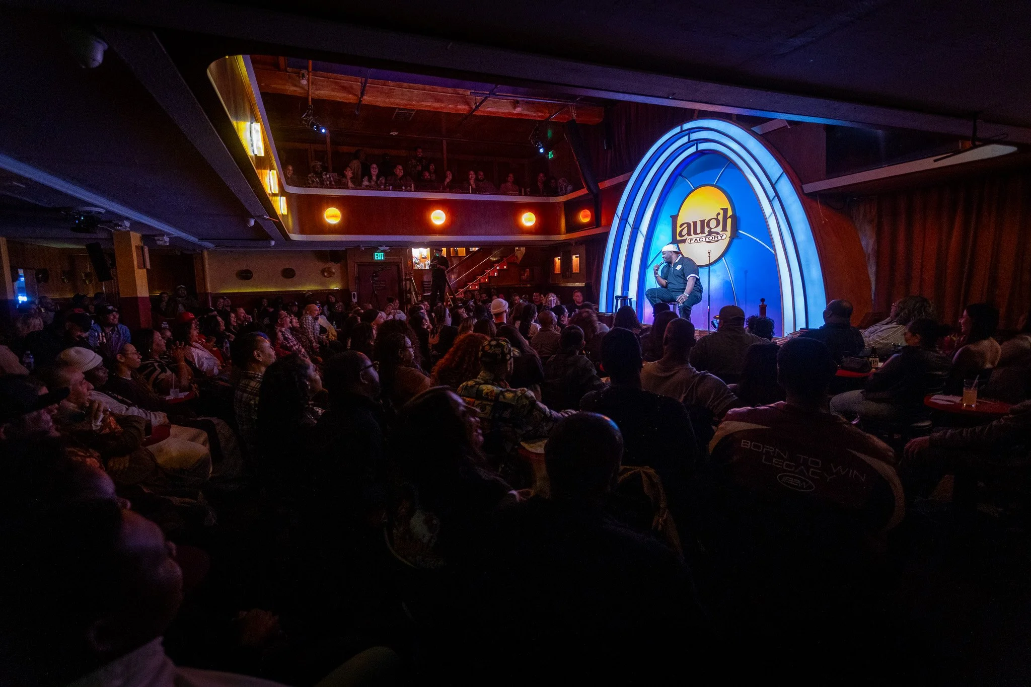 A comedian performing on stage at the Laugh Factory comedy club with an audience watching.