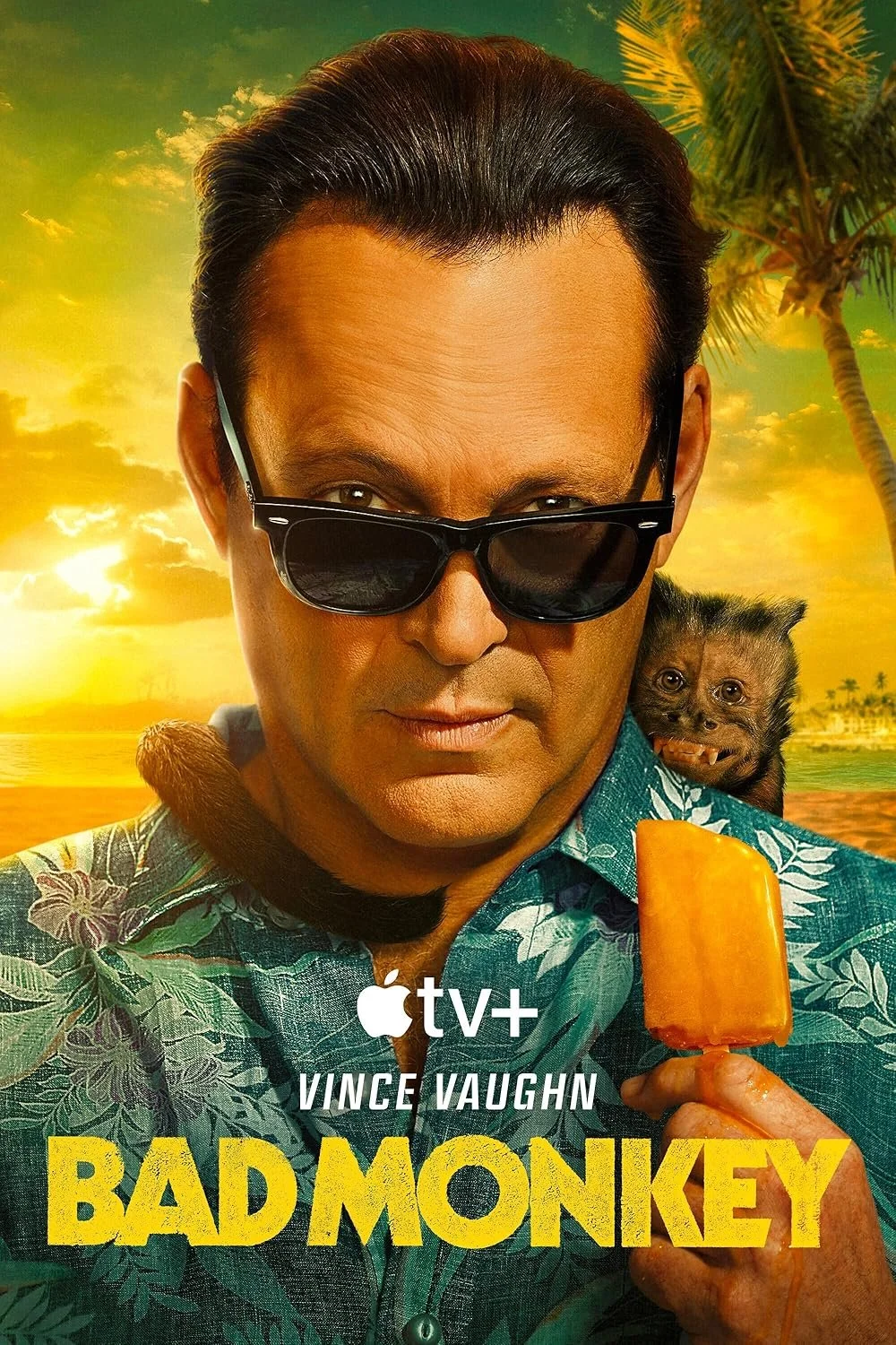 A man wearing dark sunglasses, a patterned green Hawaiian shirt, holds an orange popsicle, with a small monkey peeking over his shoulder. The background is a tropical sunset scene with palm trees and an orange-yellow sky. Text on the image says 'Apple TV+ Vince Vaughn Bad Monkey'.