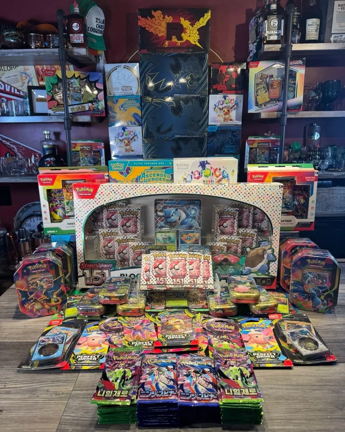 Display of Pokémon trading card game booster packs, booster boxes, and collectible tins arranged on a table in a store.