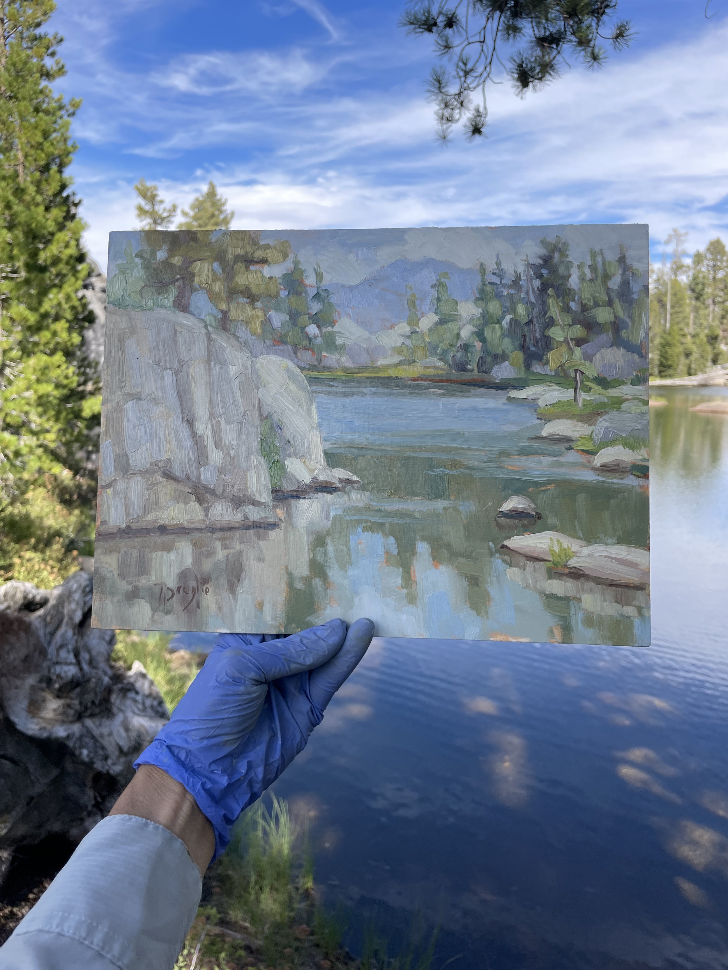 Photo of Andrea Broglio's hand holding her completed oil painting on location in front of a lake