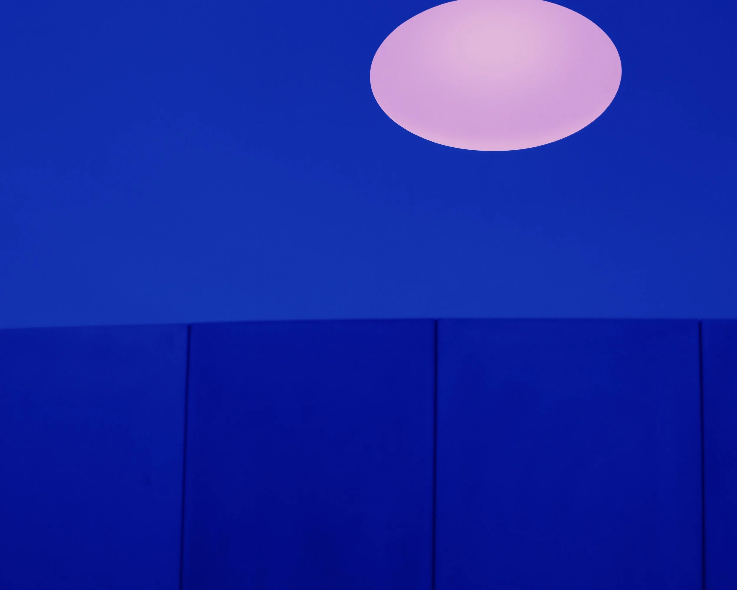 Close-up of a blue wall with a large pink circular light fixture on the upper right side.