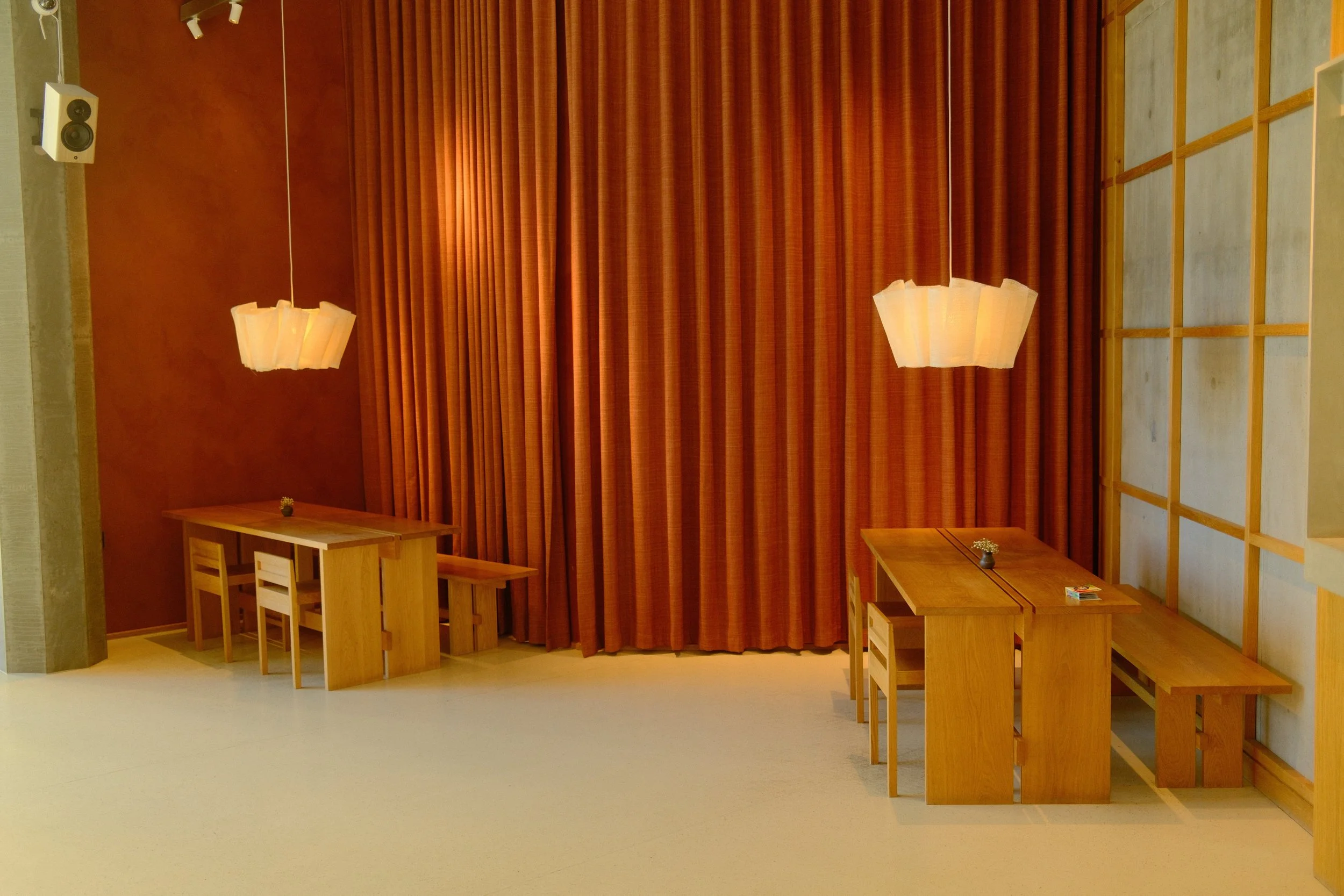 Empty wooden tables and chairs in a room with orange curtains and hanging pendant lights.