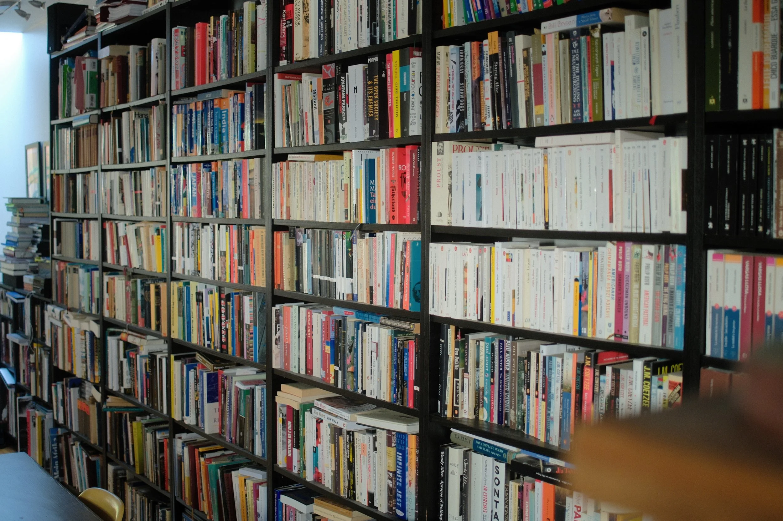 Bookshelves filled with a variety of books in a room with natural light coming from a window.