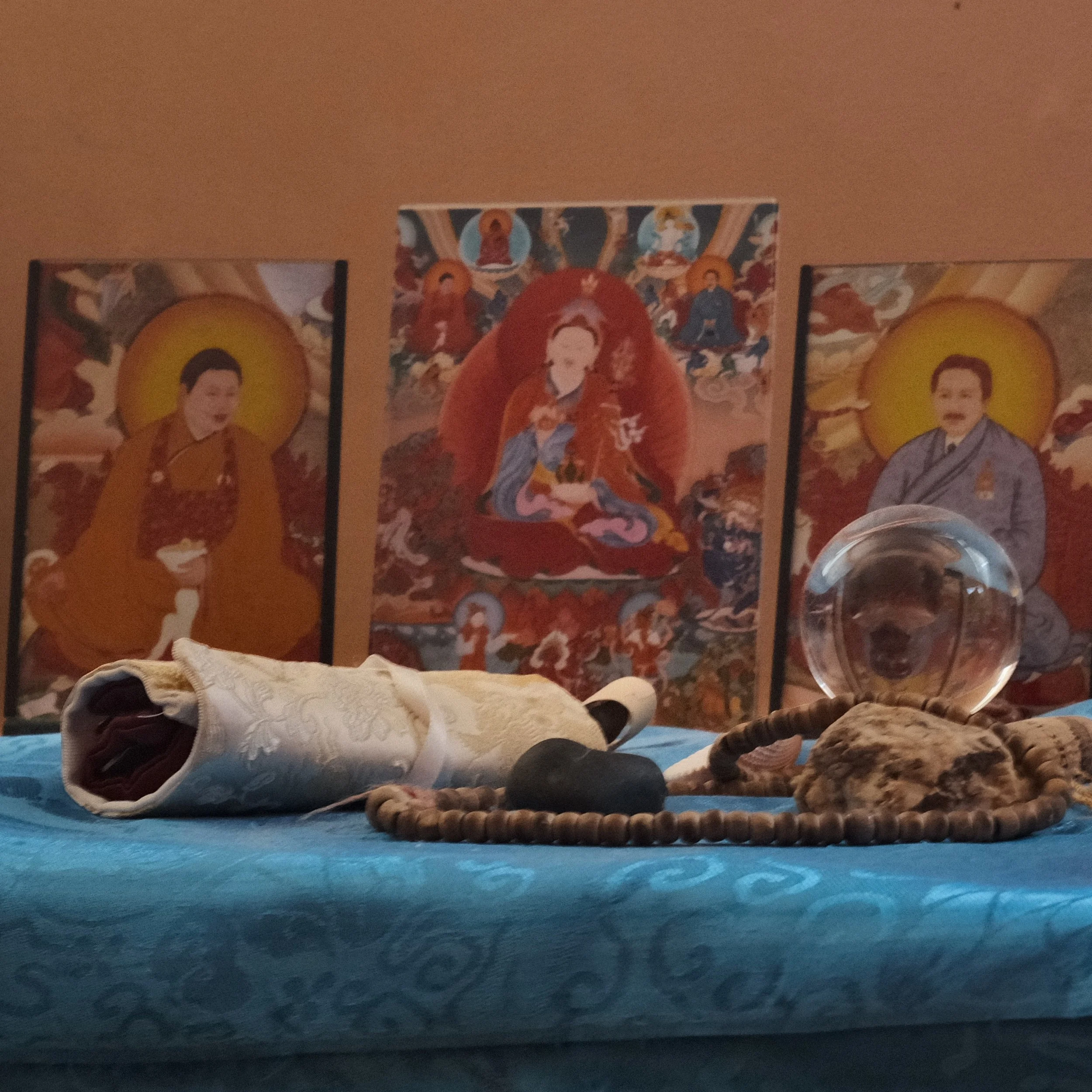 The image features several religious or spiritual posters or artwork on a wall. The artworks depict figures with a radiant halo or aura around their heads, surrounded by intricate, colorful backgrounds.
