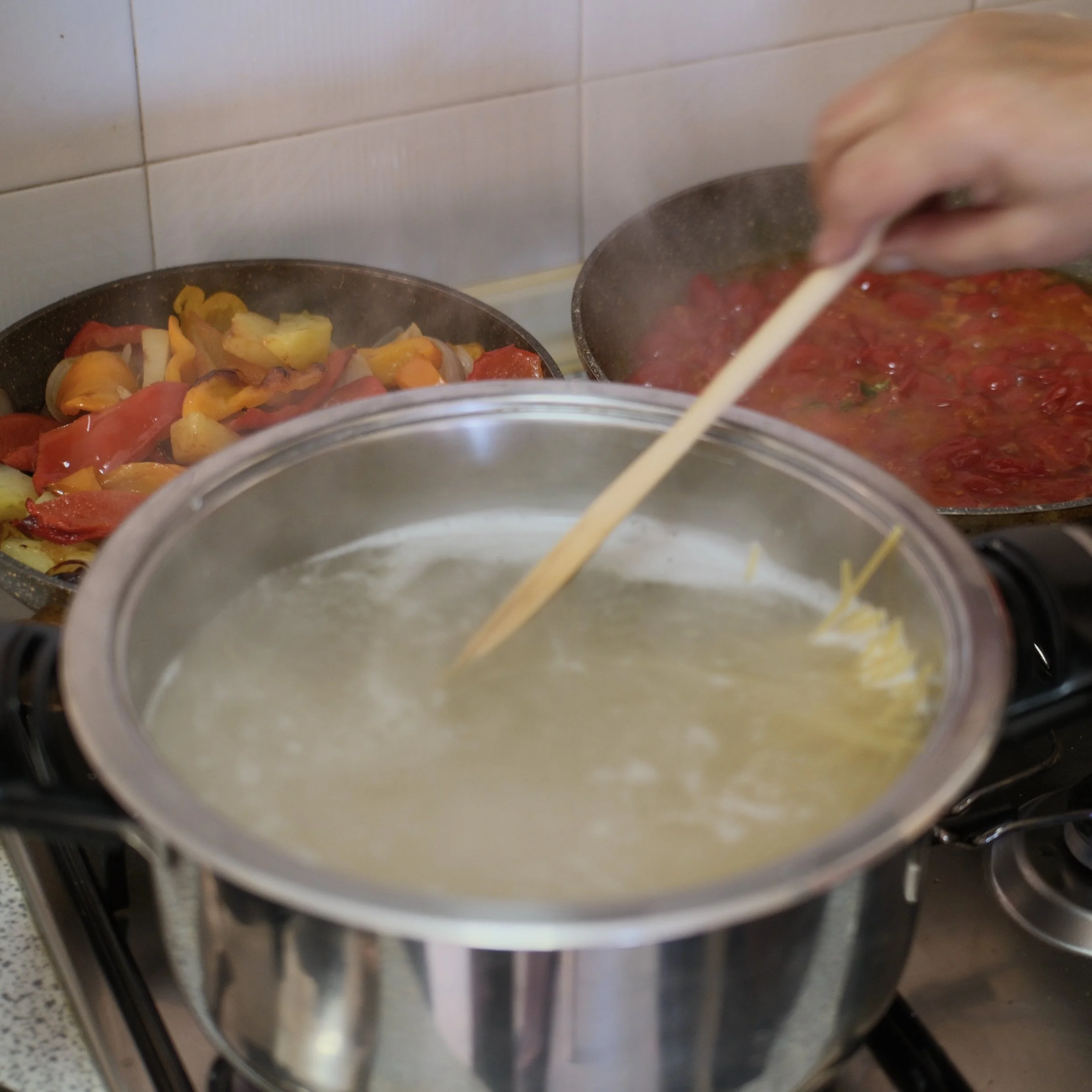 An oven with a glass door showing two pans of food inside. One pan contains roasted vegetables, and the other has a tomato-based dish, possibly sauce or stew.