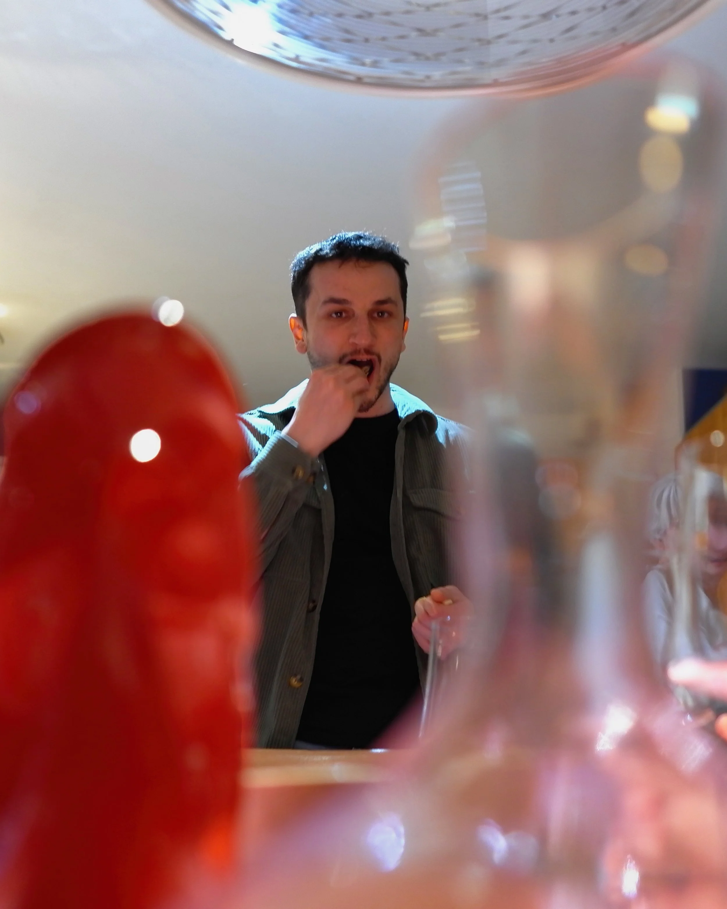A man at a table seen through a glass surface with colorful reflections, with a red object in the foreground.