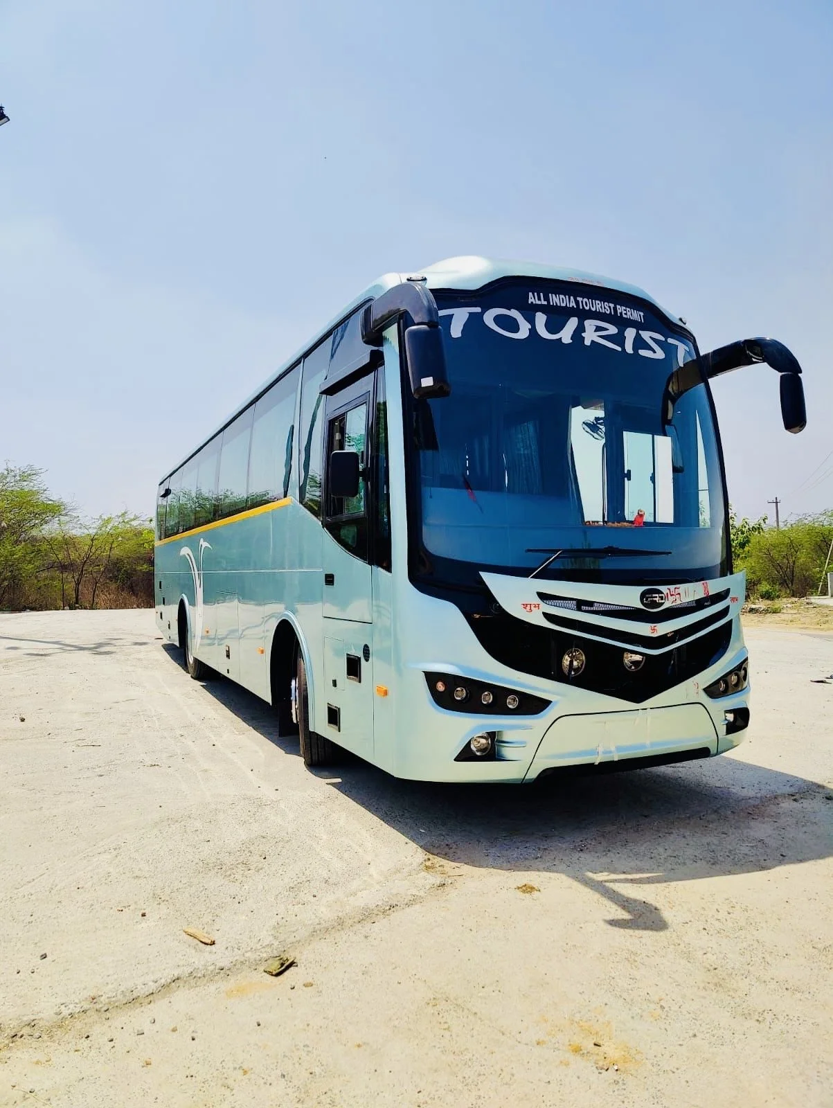 A white tour bus parked on an outdoor road with clear sky and sparse trees in the background.