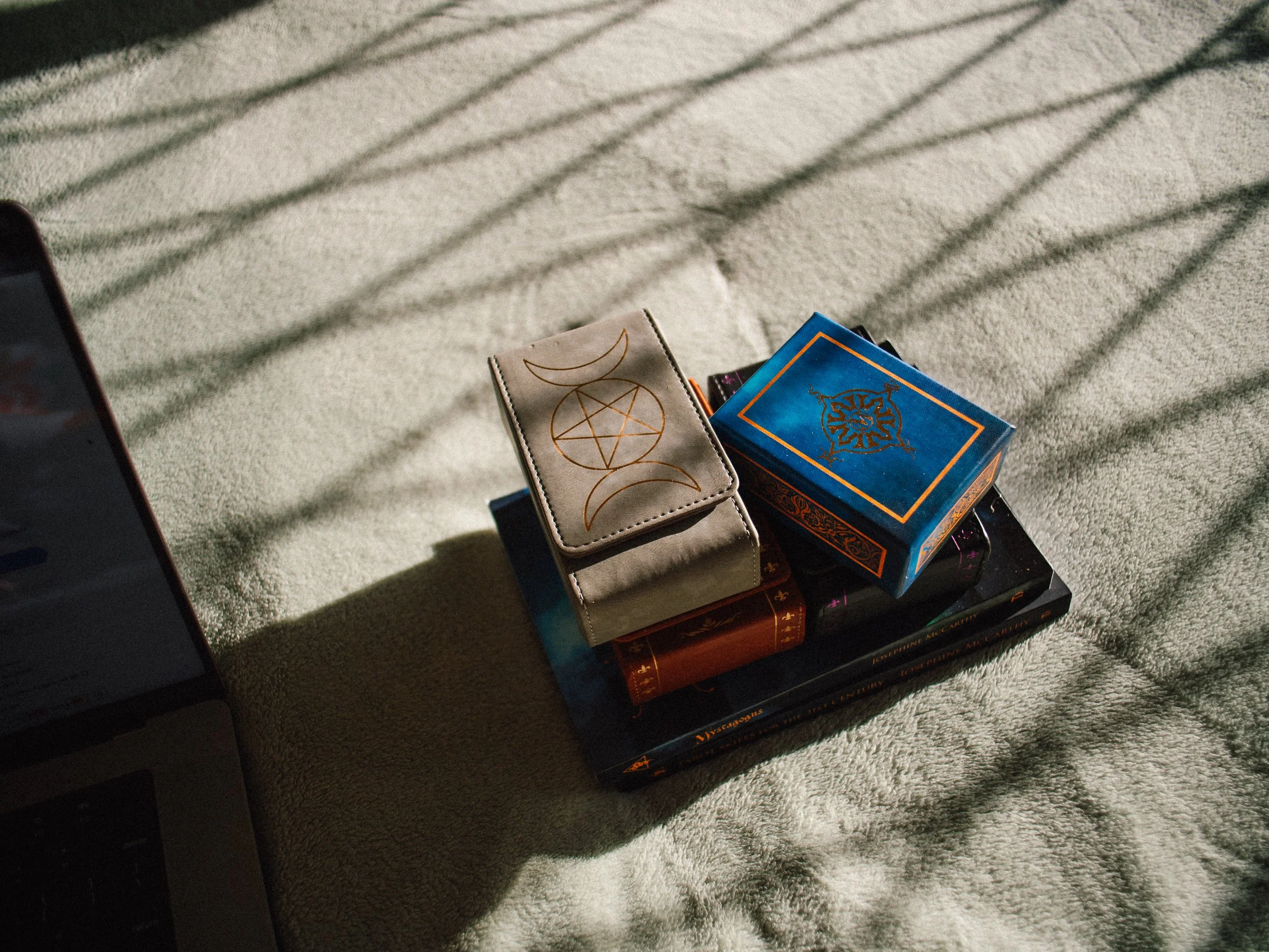 Close-up of tarot cards and a small tarot card wallet on a textured, light-colored surface. Shadows of blinds create diagonal lines across the scene.