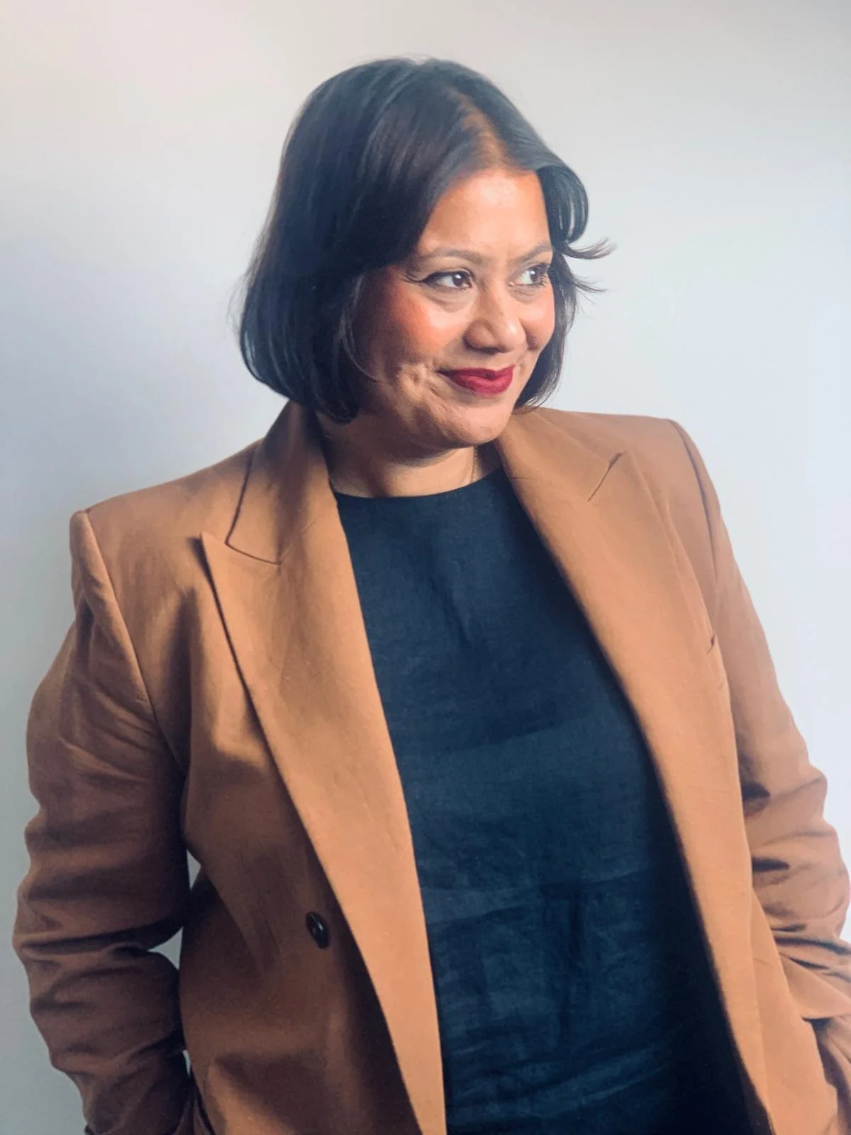 A woman with short hair in a tan suit smiling and looking to someone to her left.