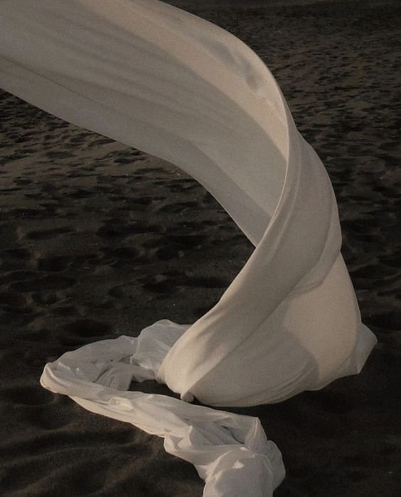 A piece of white fabric or material twisted and draped on a dark, sandy surface.