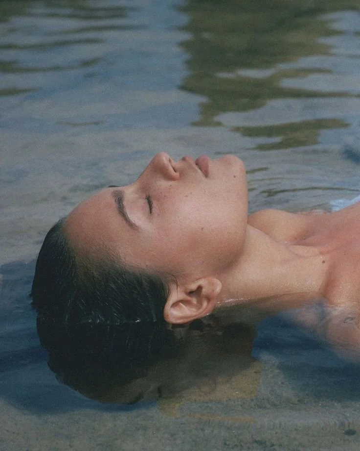 A woman with dark hair floating in water with her eyes closed
