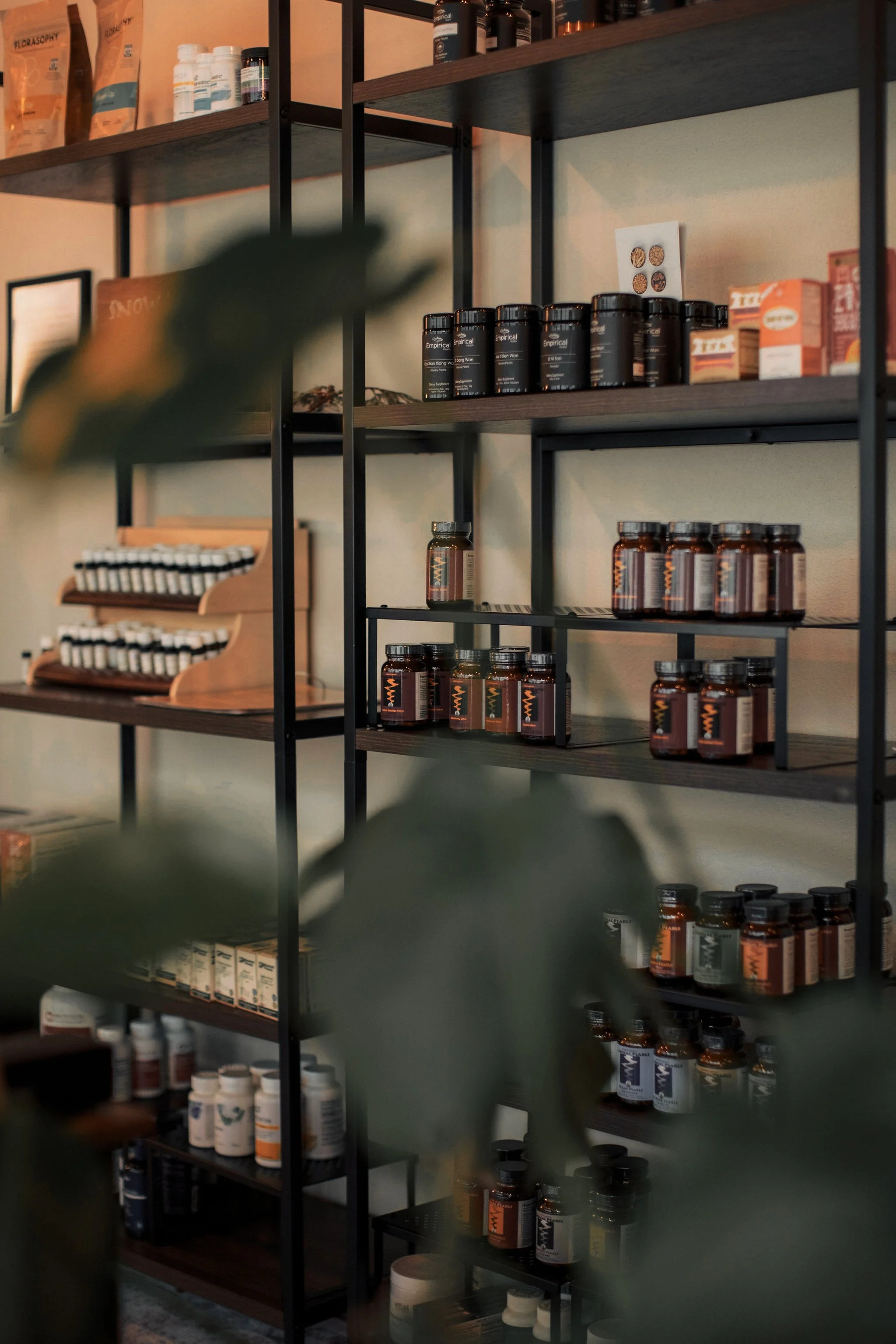 Shelves filled with supplement bottles and boxes, with some labels partially visible. The shelves are made of dark wood and black metal frame, with an assortment of containers of health-related products.