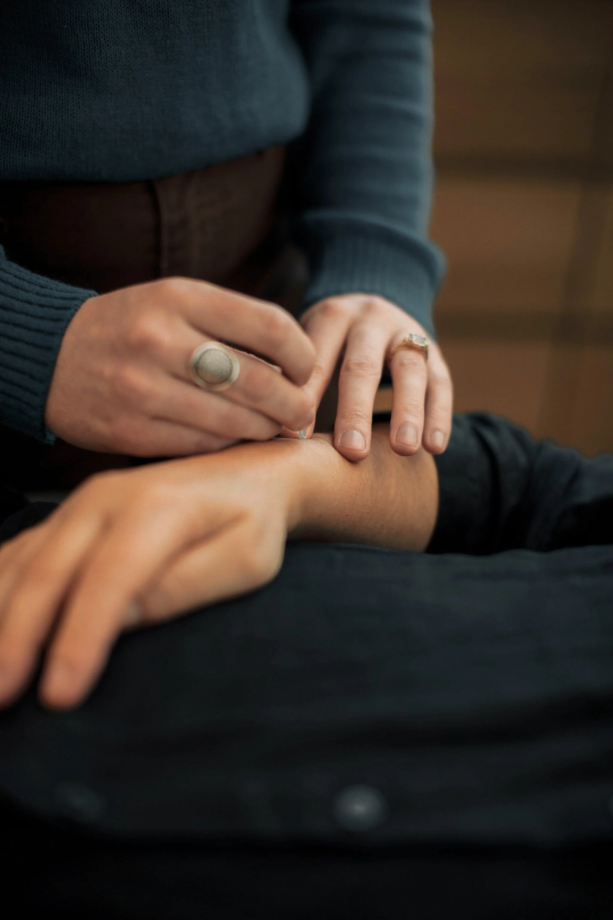 Close-up of hands with rings, one hand being held by another, against a dark background.