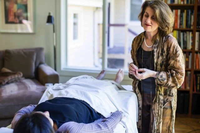A woman standing by a hospital bed talking to a patient lying in bed at home.