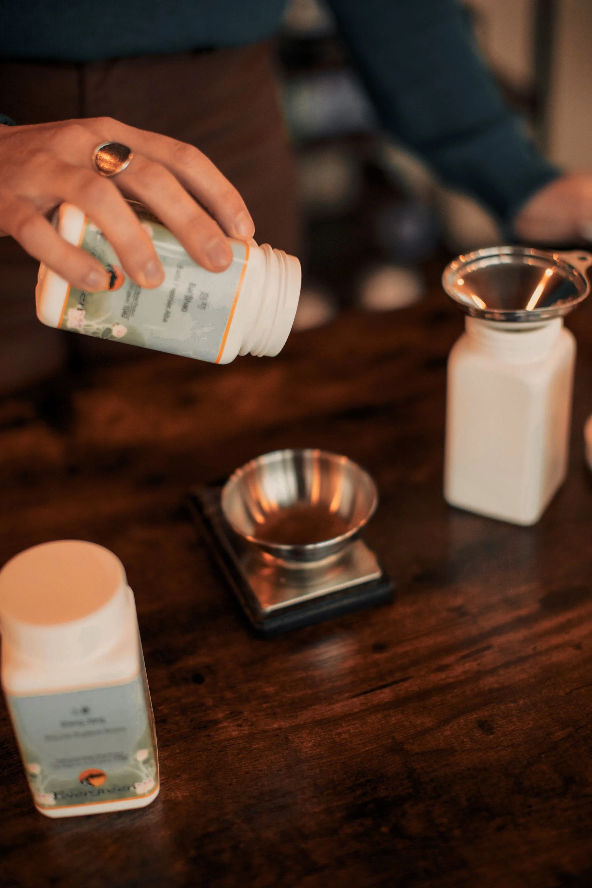 Person pouring vitamin or supplement pills into a pill dispenser on a wooden table.