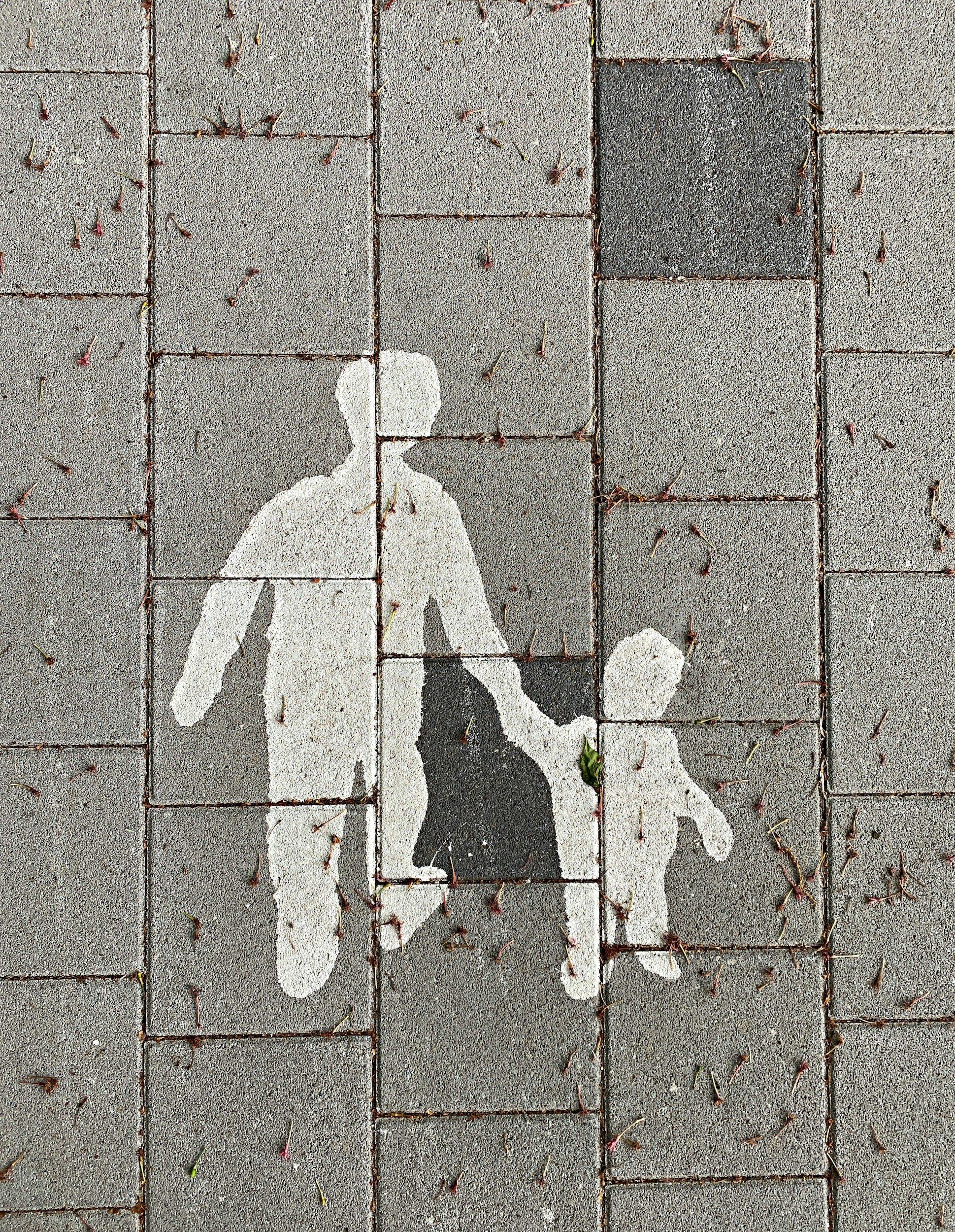 White and black painted pedestrian walking symbol on gray brick sidewalk.