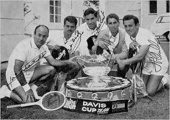 Cinco jugadores de tenis en uniforme con raquetas, celebrando con un trofeo en un ambiente de competencia deportiva.
