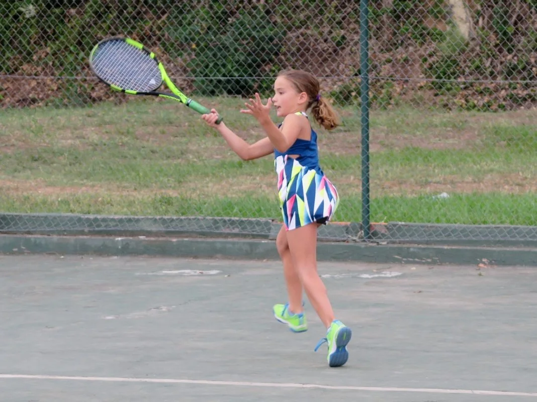 Una niña jugando al tenis en una cancha al aire libre.
