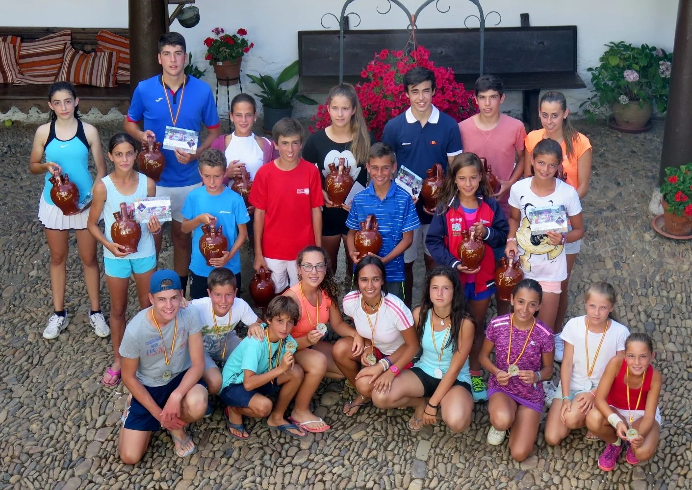 Grupo de niños y adolescentes posando con trofeos y medallas en un patio de piedra, celebrando una competencia o evento deportivo.