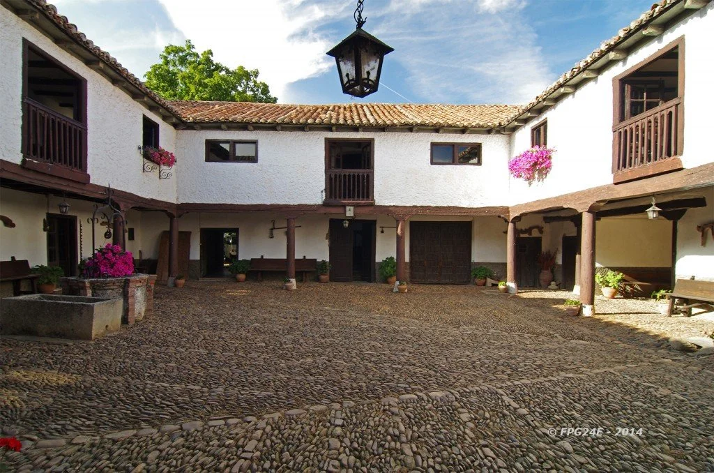 Patio interior de una vivienda tradicional con paredes blancas, techos de teja, columnas de madera y balcones con flores.