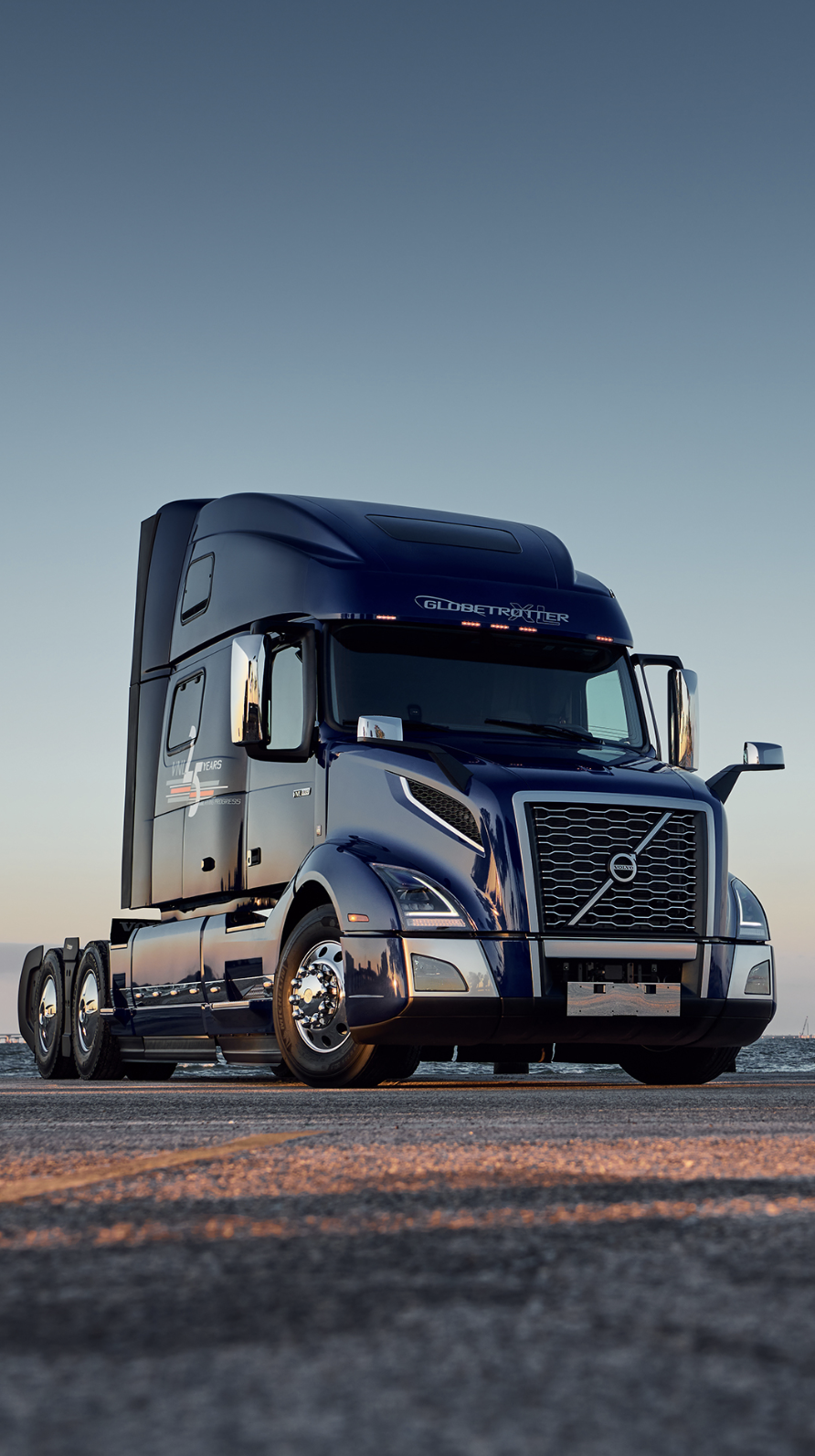 A sleek black semi-truck parked on a paved surface at dusk with a cloudy sky in the background.