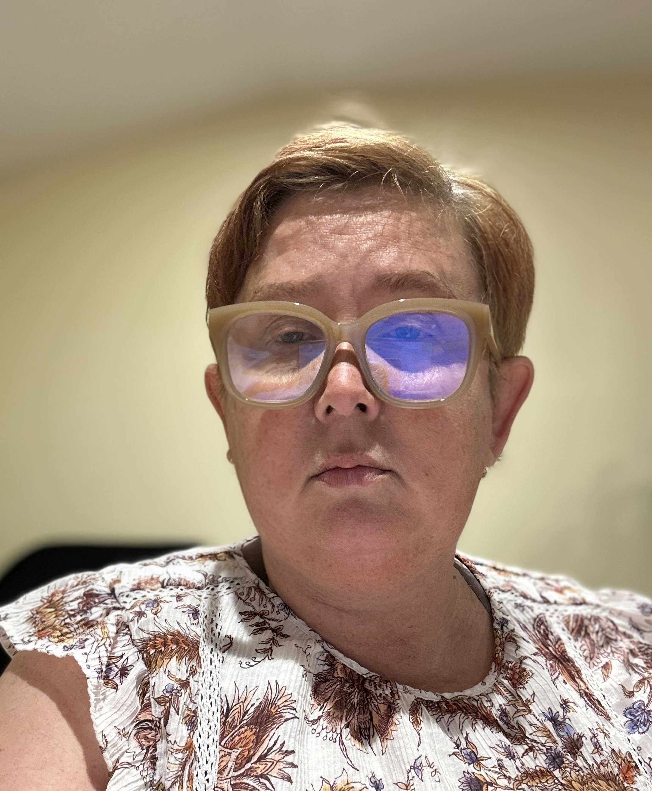 Close-up of a person wearing colorful glasses, with hair visible and wearing a patterned shirt with floral designs.