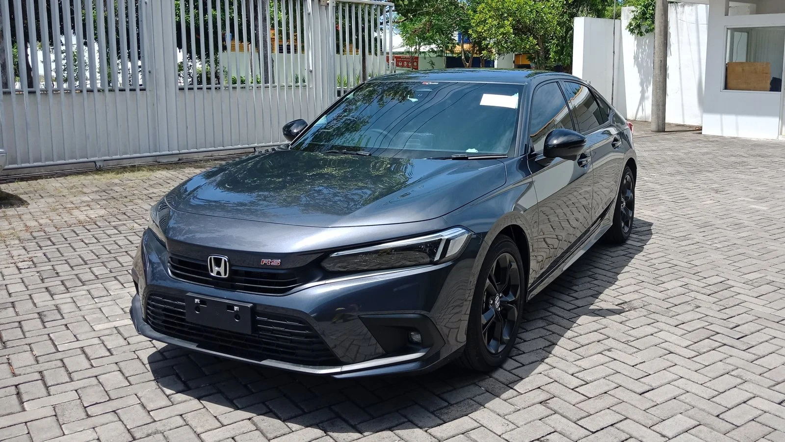 A dark gray Honda Civic RS parked on a cobblestone driveway, with a white fence and trees in the background.