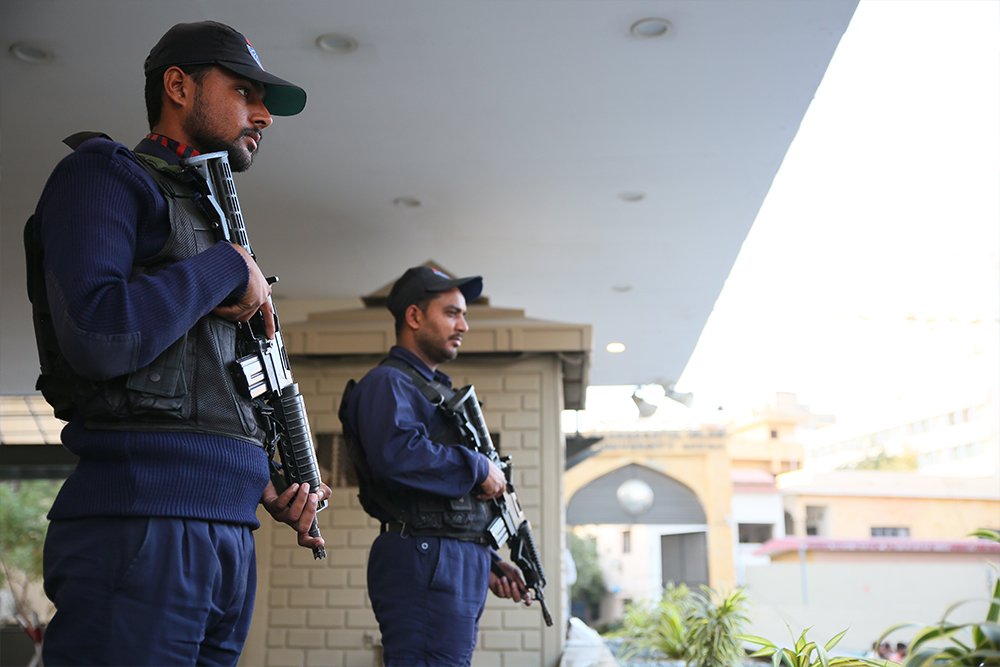 Two police officers in uniform standing guard with rifles on a porch, overlooking a residential area.