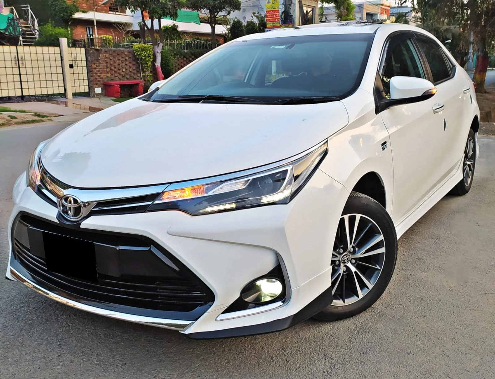 A white Toyota sedan parked on a street with trees and buildings in the background.