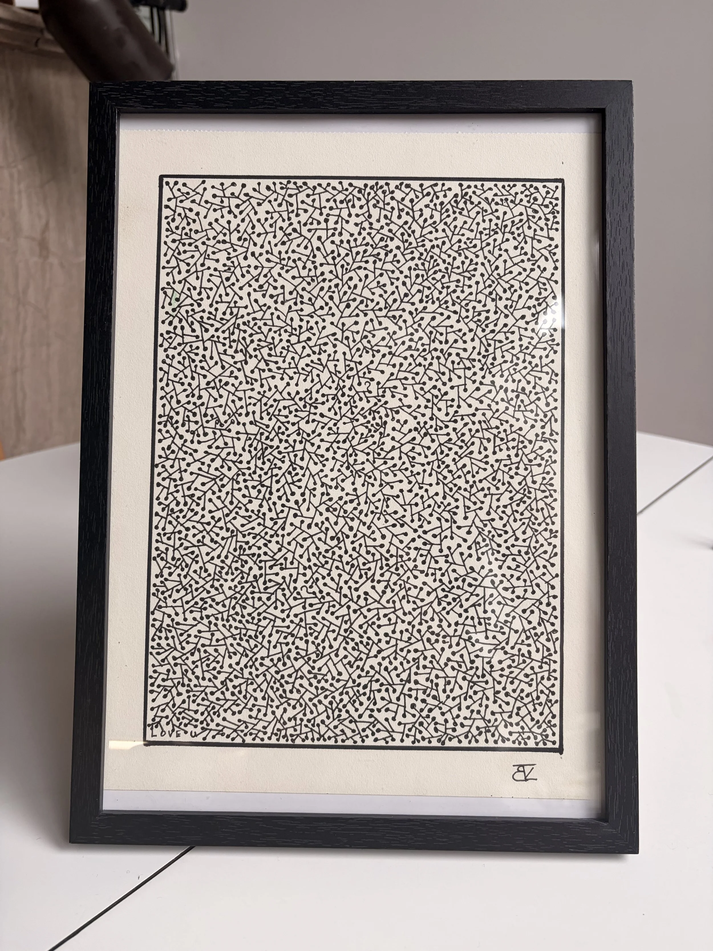 A framed piece of art featuring a dense black and white pattern of lines and dots, with the word 'LOVE' subtly integrated at the bottom.