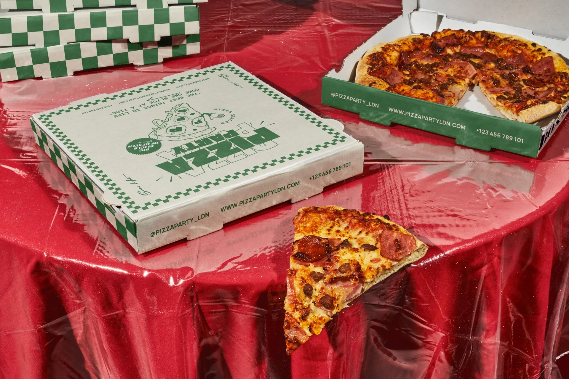 A partially eaten cheese and meat pizza in an open pizza box on a red table with a Domino's pizza box nearby. The pizza has cheese, pepperoni, and other meat toppings.