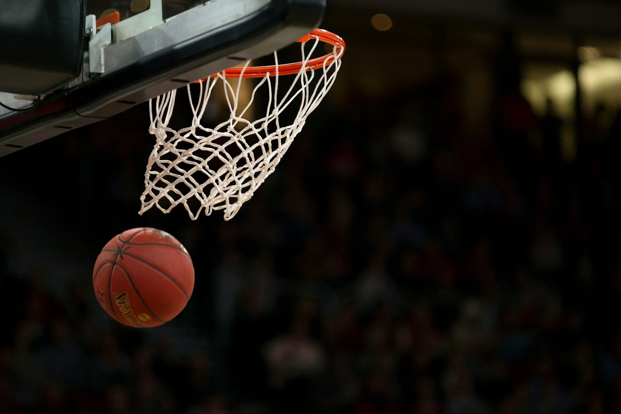 A basketball hoop with a basketball approaching the net, set against a dark background.