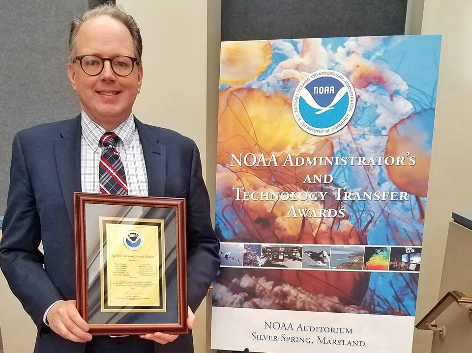 Sean Potter holding a NOAA Administrator's Award plaque and standing next to a poster that reads "NOAA Administrator's and Technology Transfer Awards"