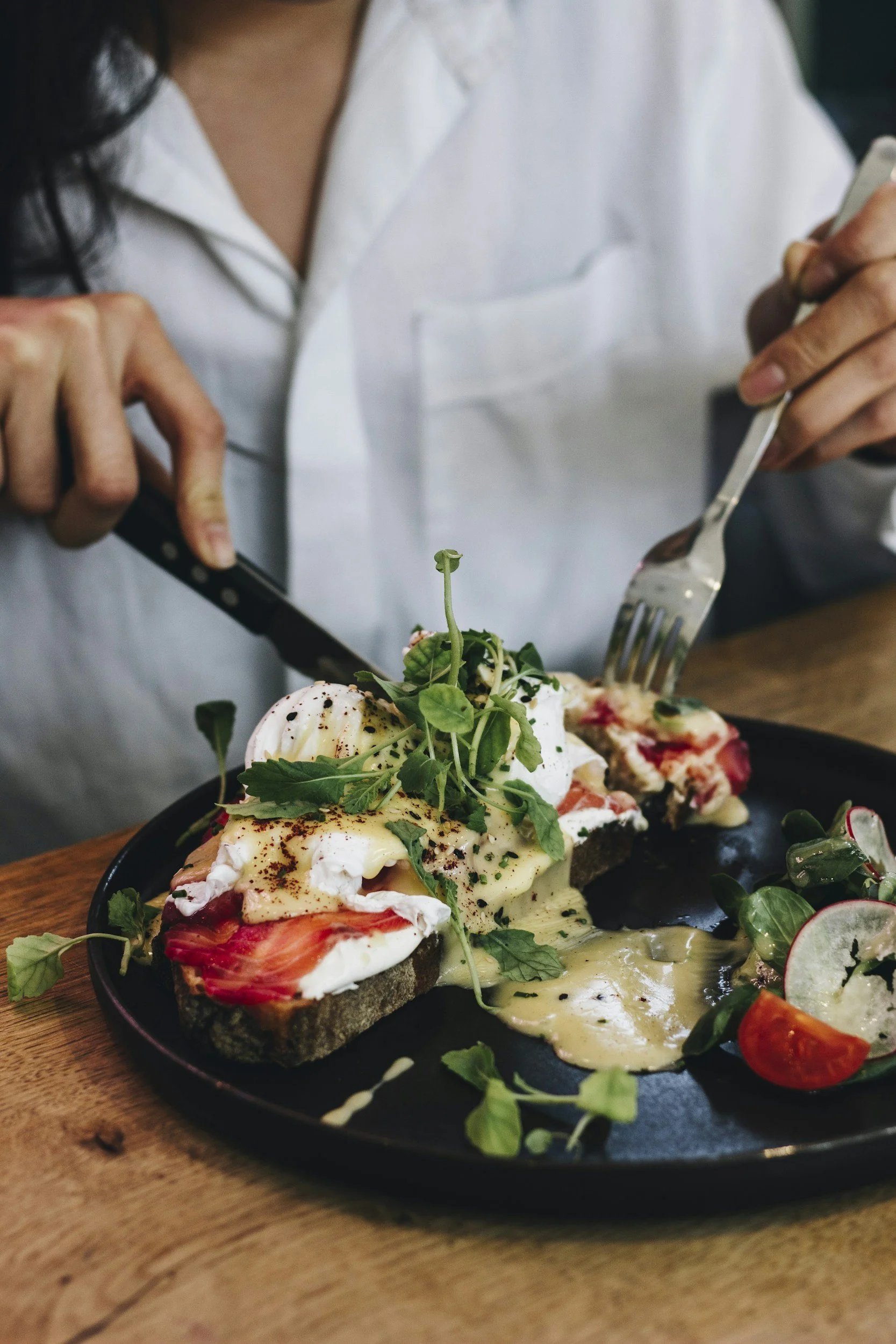 Gerecht met gepocheerd ei, tomaat, veganistische saus, microgroene planten en salade op een zwarte plaat.