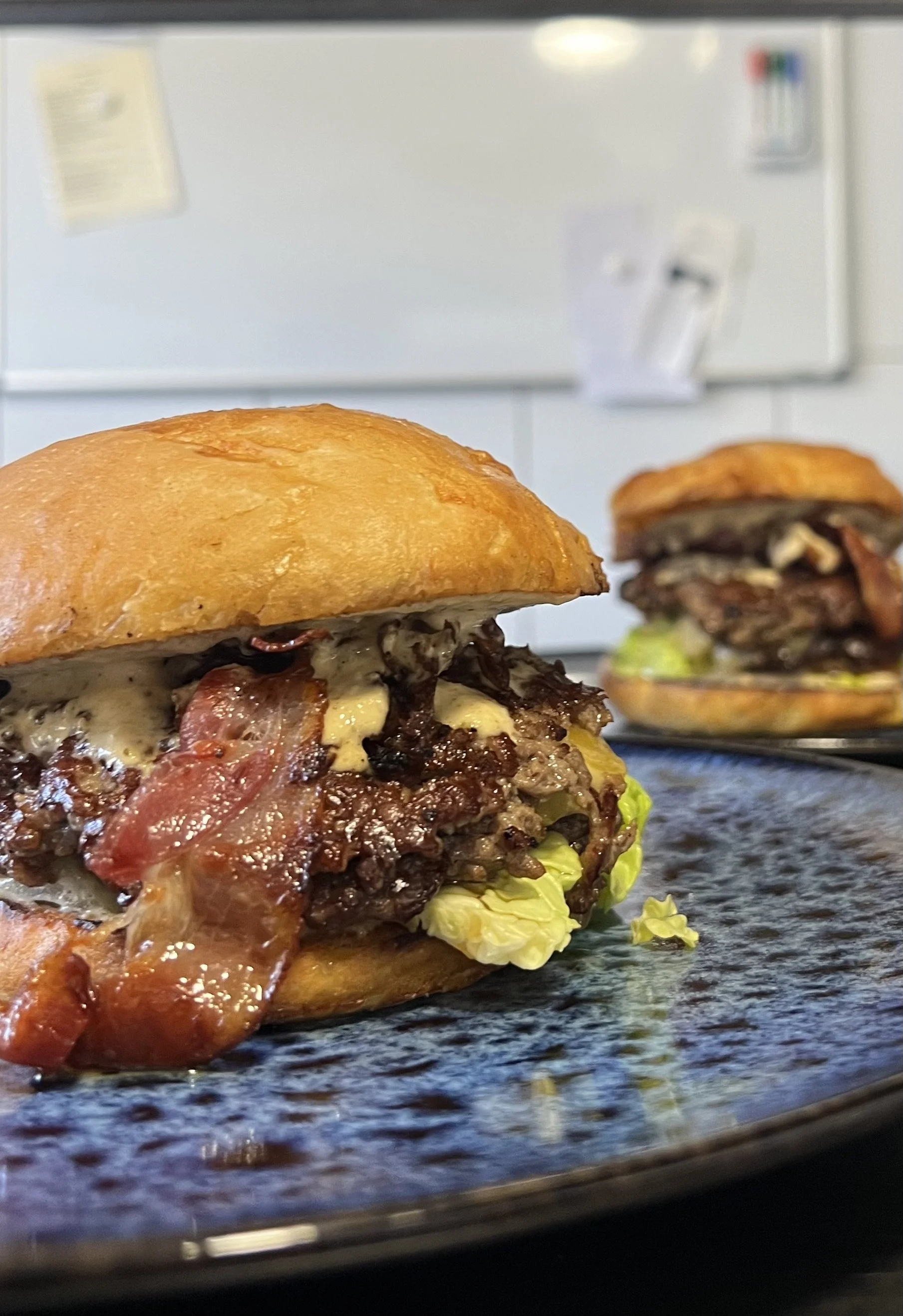Close-up van een hamburger met vlees, spek, kaas, sla en een zachte broodje, op een donkere plaat.