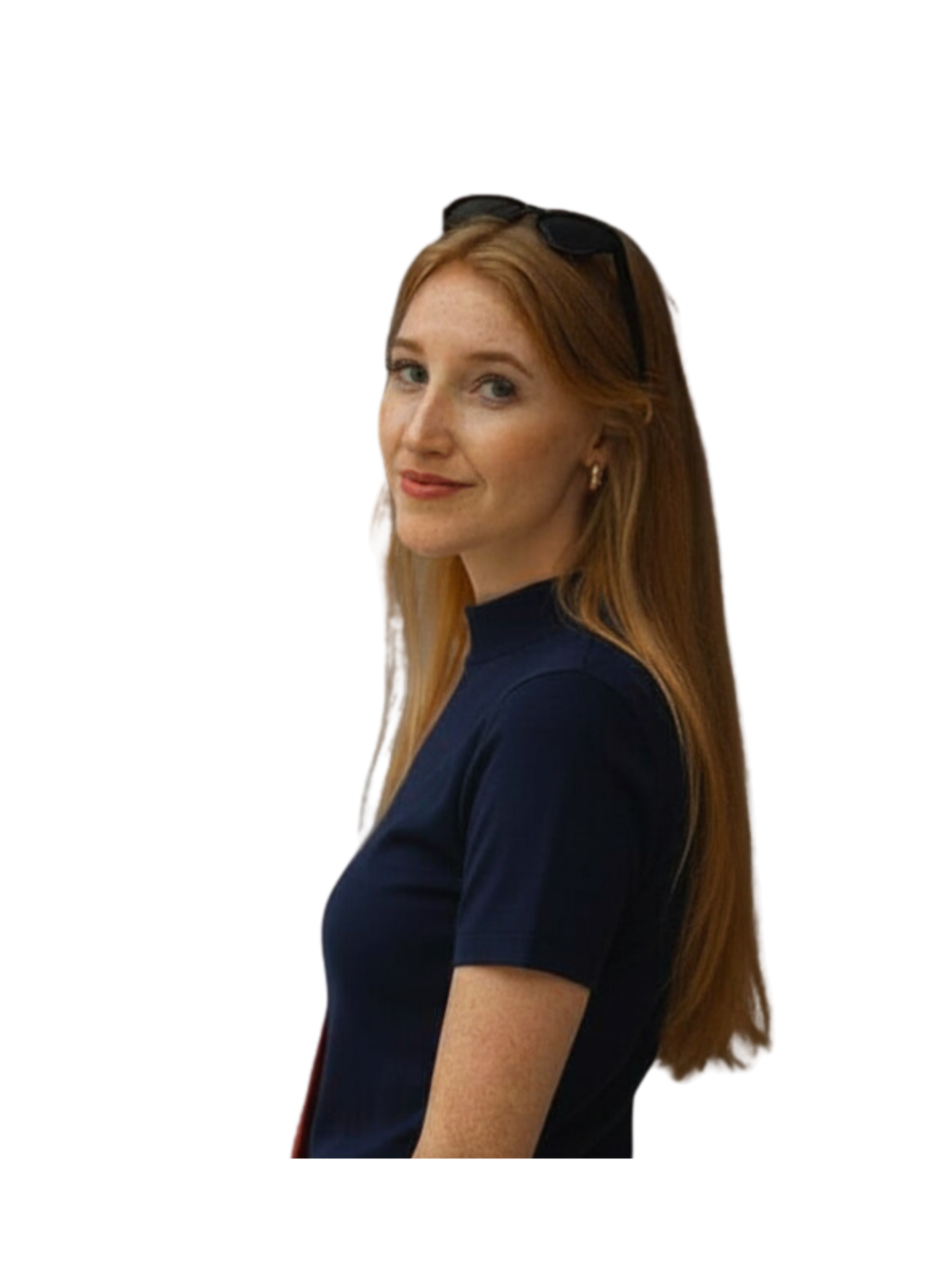 A woman with long red hair, wearing a dark top, black sunglasses on her head, and earrings, looking at the camera with a slight smile.