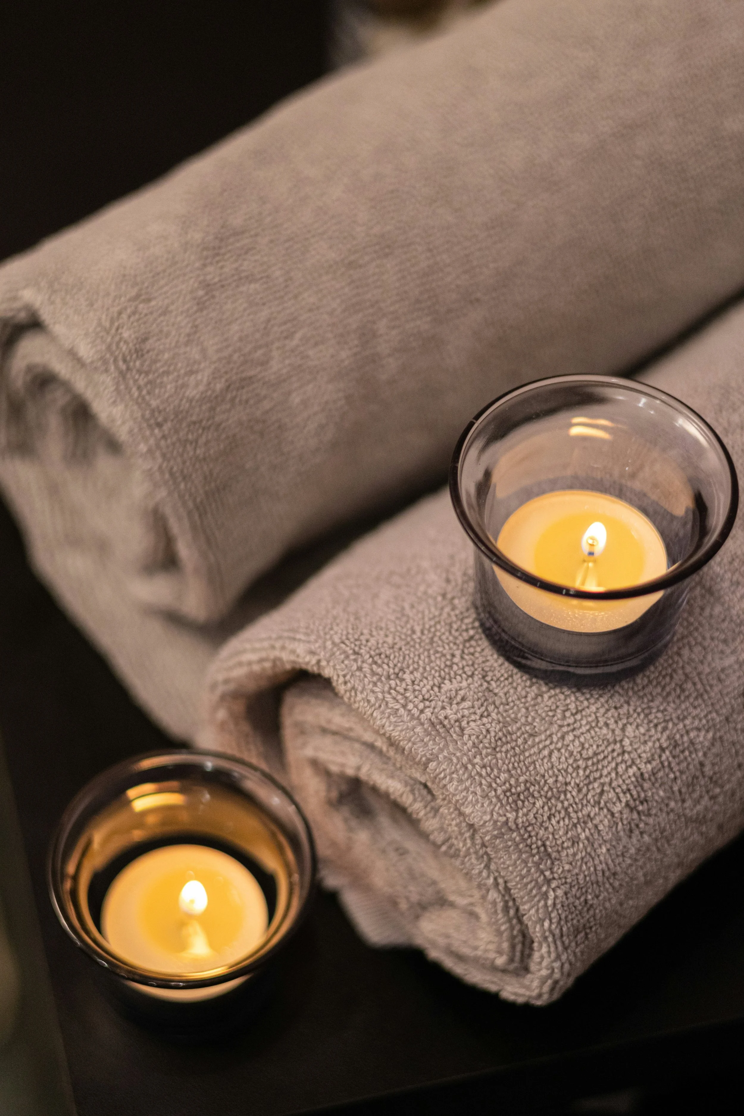 A lit yellow candle in a glass holder placed on a folded gray towel.