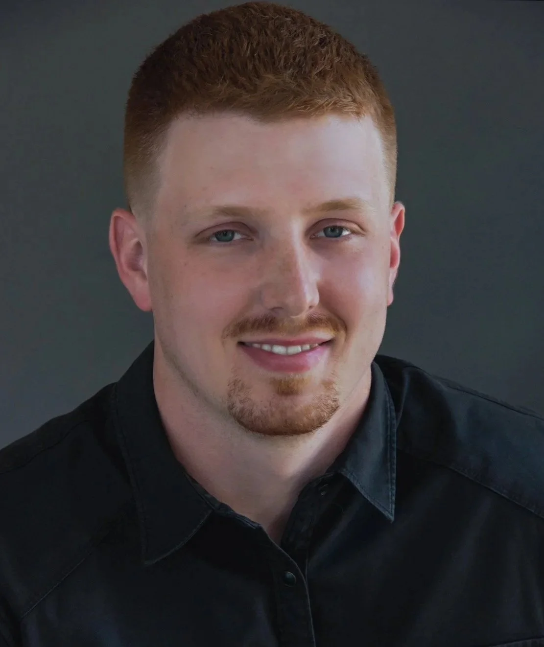 Headshot of a man with short red hair, a beard, and mustache, wearing a dark gray collared shirt, smiling slightly against a gray textured background.