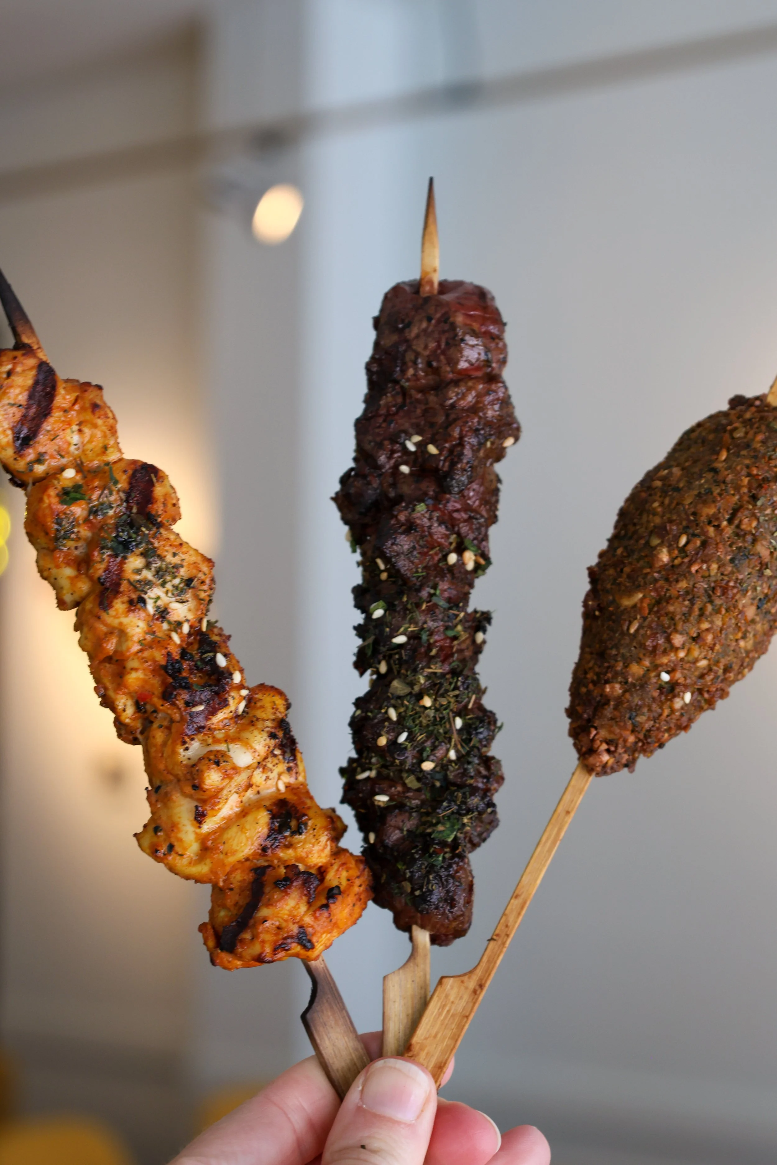 Three skewers of grilled meat, seasoned and garnished, held by a person's hand.