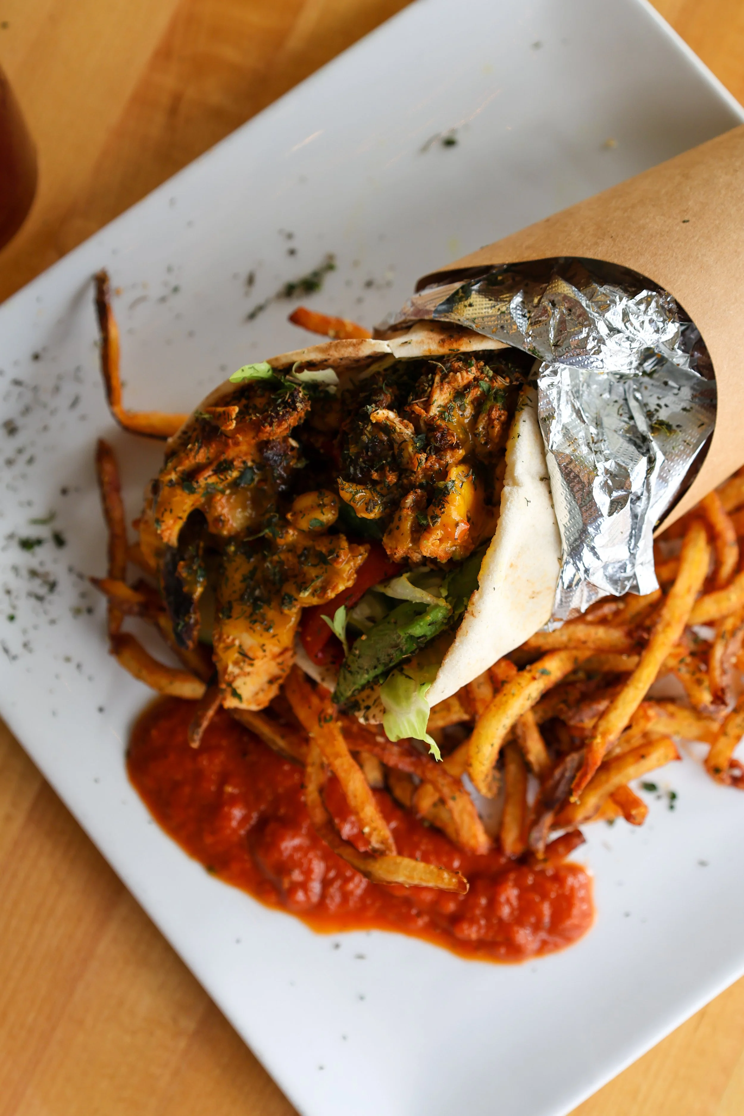 Close-up of an Indian-style wrap with grilled chicken, vegetables, and herbs, served on a white plate with tomato sauce.