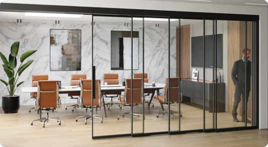 Modern conference room with a large table surrounded by tan chairs, marble wall, abstract art, and a glass wall with sliding doors. A man in a suit is near the entrance.