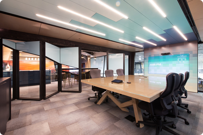 Modern conference room with a large wooden table, multiple black office chairs, and a digital screen displaying the time 4:08 PM. The room has glass partitions and a ceiling with sleek, linear lighting.