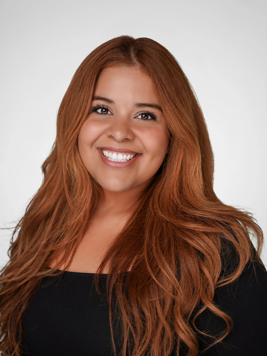 A smiling woman with long, wavy red hair wearing a black top against a plain white background.
