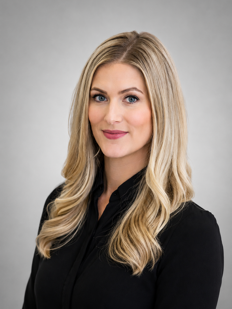 A woman with long, blonde hair and blue eyes wearing a black top, smiling at the camera against a neutral gray background.