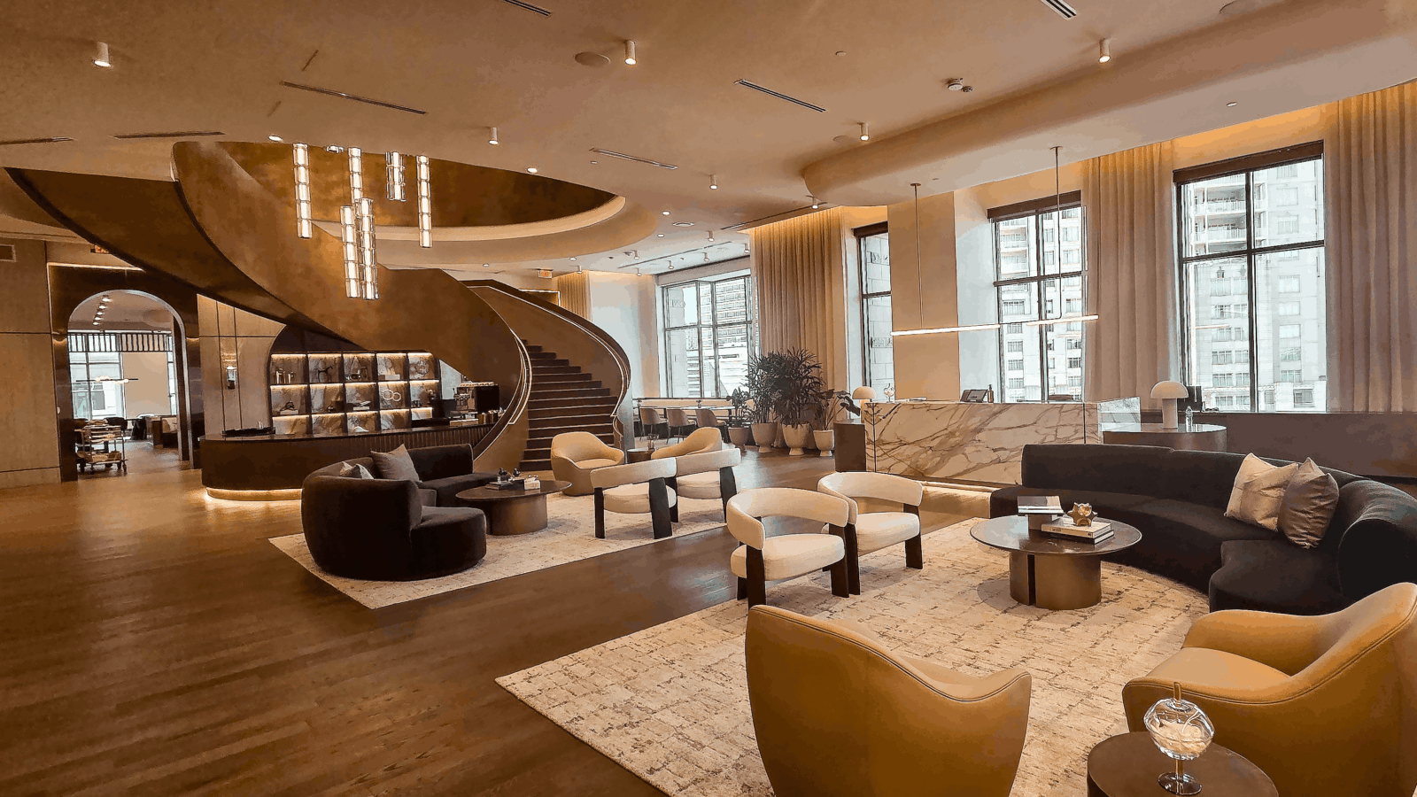 Elegant hotel lobby with modern seating, large windows, a marble reception desk, and a spiral staircase